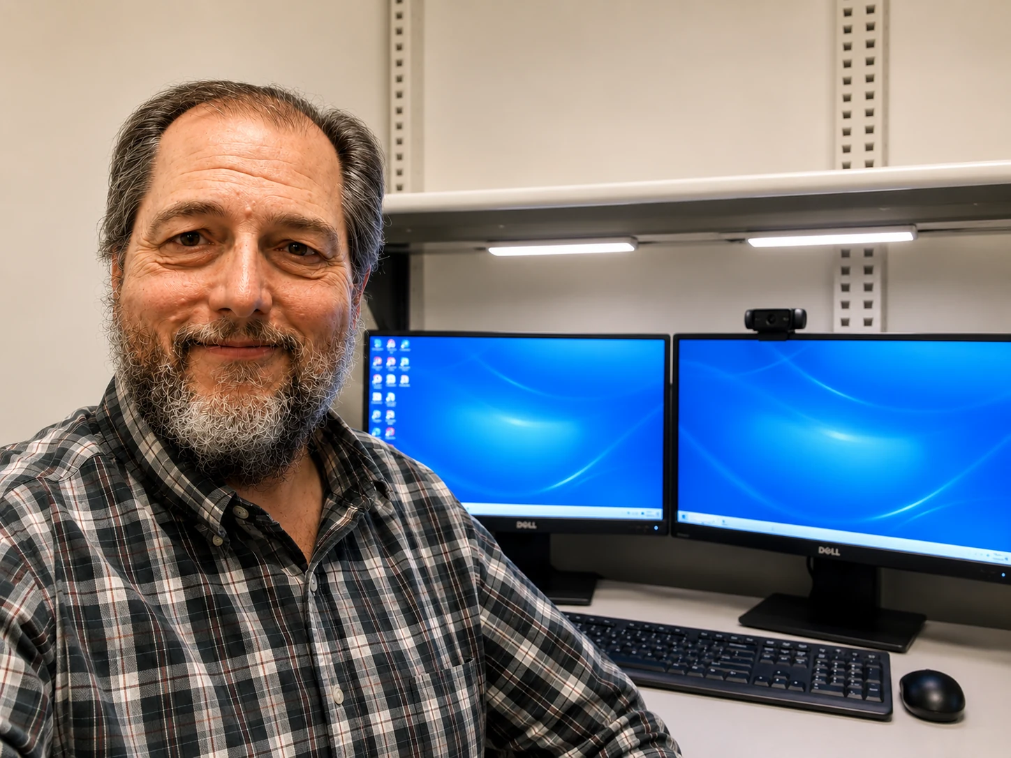Tom Backus smiling in his workspace with dual monitors behind him.